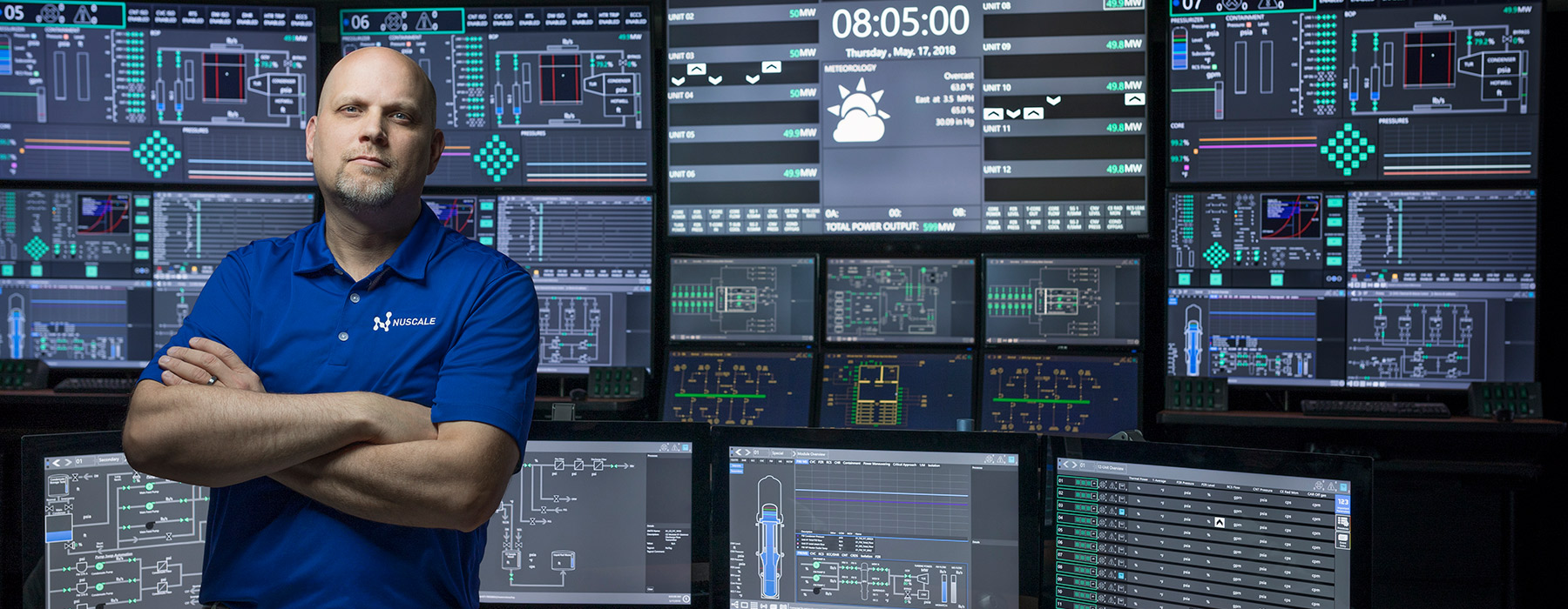 NuScale employee standing with arms crossed in front of multiple monitors. 
