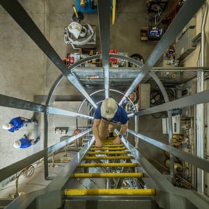 NuScale employee climbing up ladder in industrial setting.