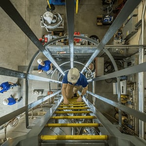 NuScale working climbing up ladder in industrial setting.